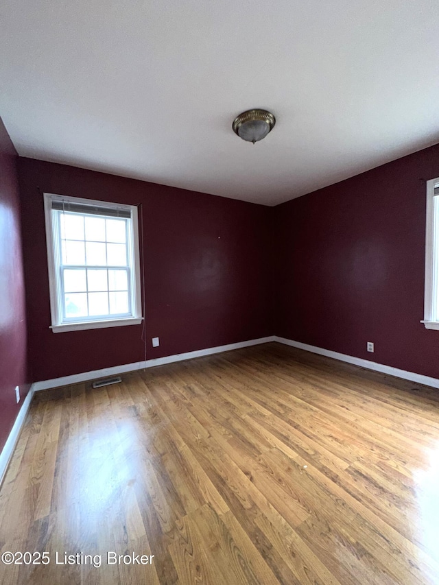 empty room with light wood-type flooring, visible vents, and baseboards