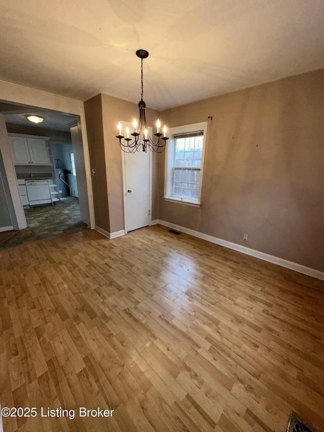 unfurnished dining area featuring visible vents, a notable chandelier, baseboards, and wood finished floors