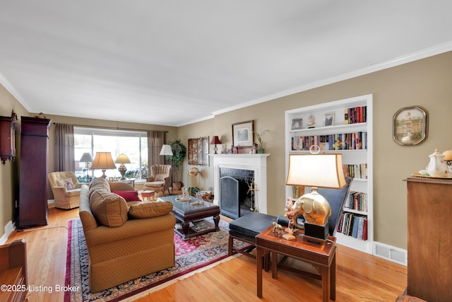 living room with ornamental molding, light wood-type flooring, built in features, and a tiled fireplace