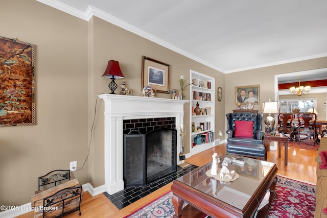 living room featuring a tiled fireplace, an inviting chandelier, ornamental molding, wood-type flooring, and built in features