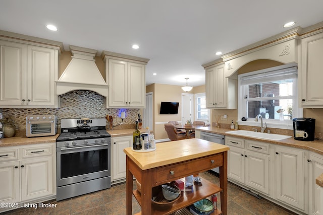 kitchen featuring appliances with stainless steel finishes, hanging light fixtures, cream cabinetry, sink, and custom exhaust hood