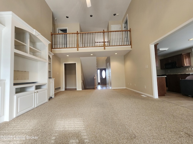 unfurnished living room with ceiling fan, a high ceiling, and light carpet