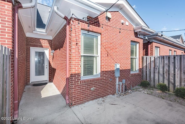 view of side of property featuring brick siding, fence, and a patio