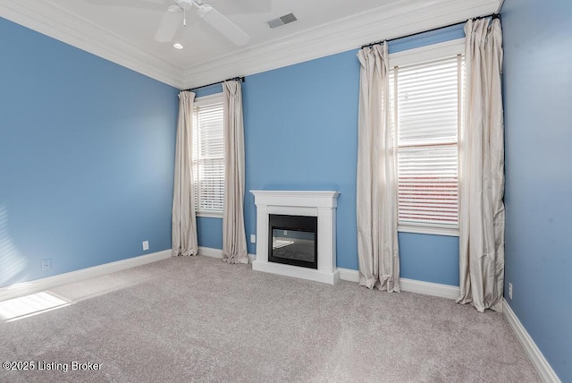 unfurnished living room with light colored carpet, visible vents, ornamental molding, a glass covered fireplace, and baseboards