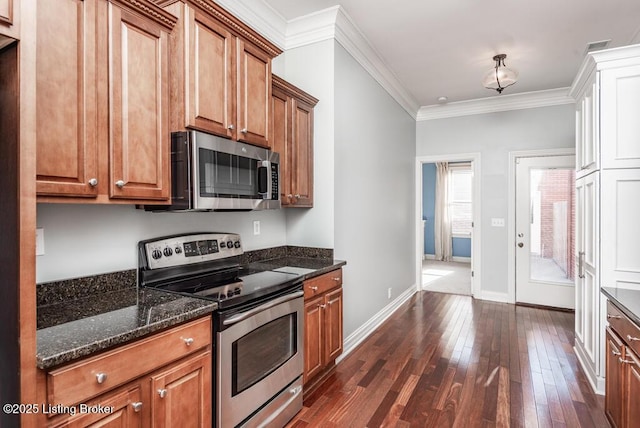 kitchen featuring brown cabinetry, appliances with stainless steel finishes, dark wood-type flooring, dark stone countertops, and crown molding