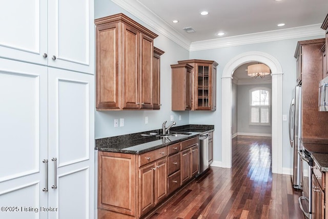 kitchen featuring arched walkways, glass insert cabinets, appliances with stainless steel finishes, ornamental molding, and a sink