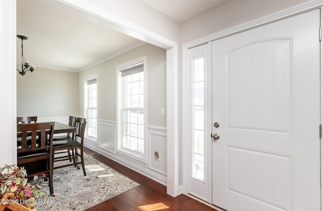 foyer featuring wainscoting, ornamental molding, dark wood-type flooring, a decorative wall, and a notable chandelier