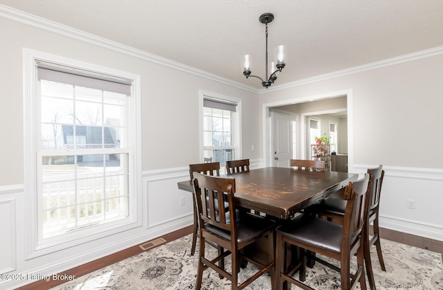 dining room with crown molding, a notable chandelier, visible vents, wainscoting, and wood finished floors