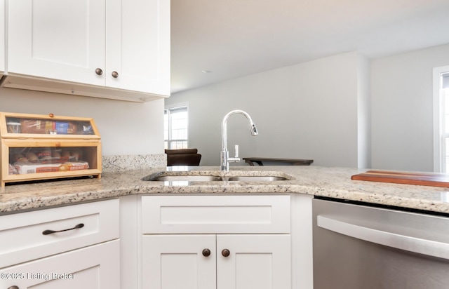 kitchen with light stone counters, white cabinetry, a sink, and stainless steel dishwasher