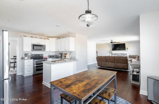 kitchen featuring dark wood finished floors, open floor plan, a peninsula, stainless steel appliances, and white cabinetry