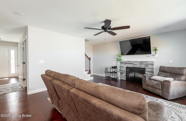 living area featuring a fireplace, a ceiling fan, baseboards, stairway, and dark wood-style floors