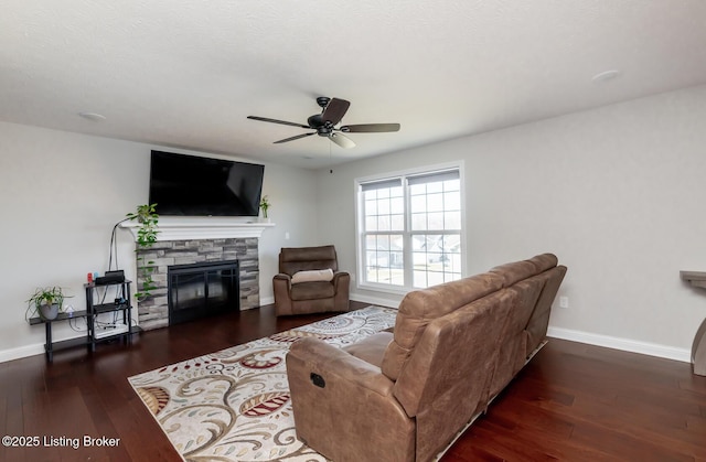 living room with ceiling fan, baseboards, wood finished floors, and a stone fireplace