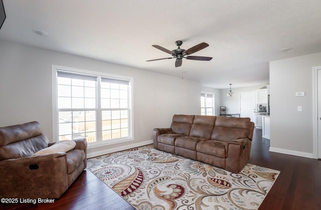 living area with a ceiling fan, baseboards, and dark wood-type flooring