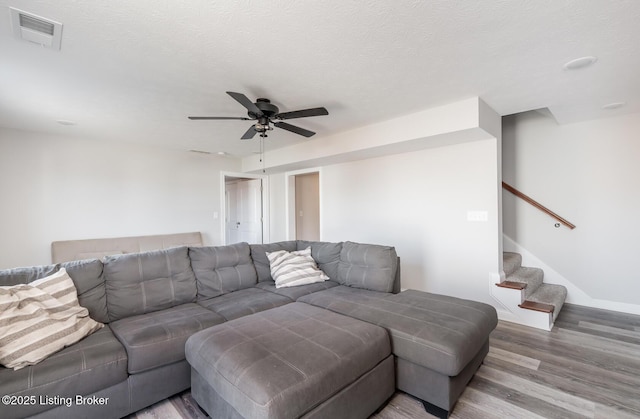 living area featuring visible vents, stairway, ceiling fan, a textured ceiling, and wood finished floors