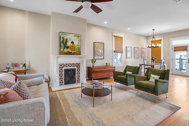 living room with a tiled fireplace, light hardwood / wood-style floors, and ceiling fan with notable chandelier