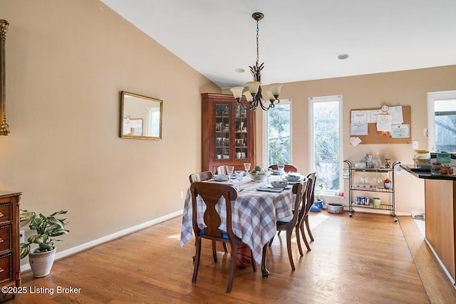 dining area featuring a notable chandelier, vaulted ceiling, baseboards, and light wood-style floors