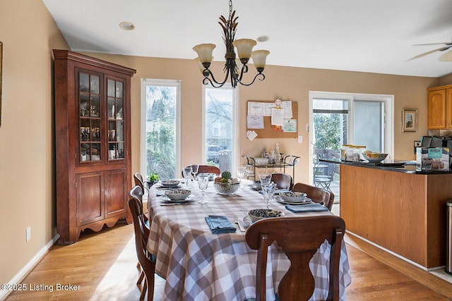 dining area with light wood-type flooring, a wealth of natural light, baseboards, and ceiling fan with notable chandelier