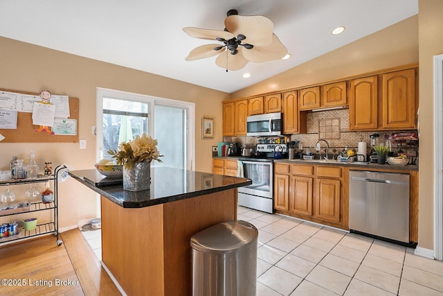 kitchen featuring a kitchen island, backsplash, vaulted ceiling, stainless steel appliances, and a sink