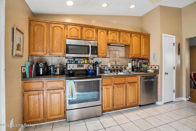 kitchen with lofted ceiling, a sink, appliances with stainless steel finishes, brown cabinets, and dark countertops