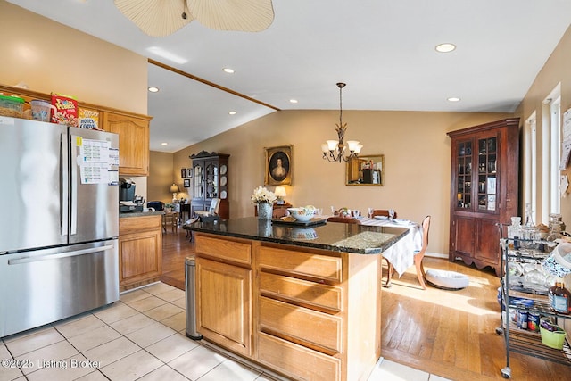 kitchen featuring freestanding refrigerator, a center island, brown cabinetry, dark stone countertops, and pendant lighting