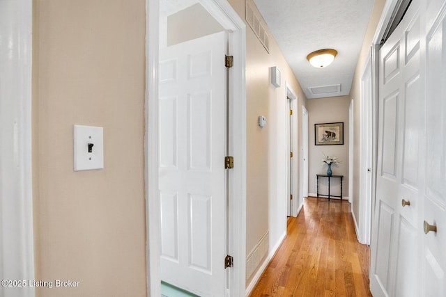 hallway featuring a textured ceiling, visible vents, baseboards, light wood-type flooring, and attic access