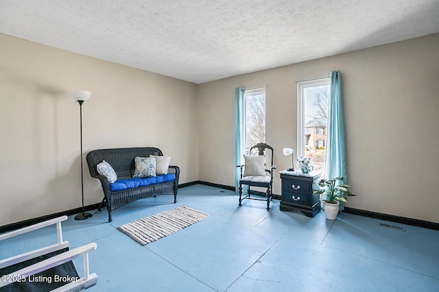 sitting room with a textured ceiling, concrete flooring, visible vents, and baseboards