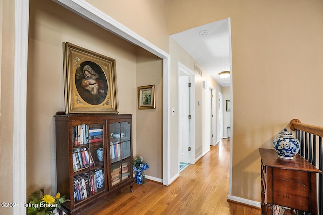 hall featuring light wood-type flooring, visible vents, and baseboards