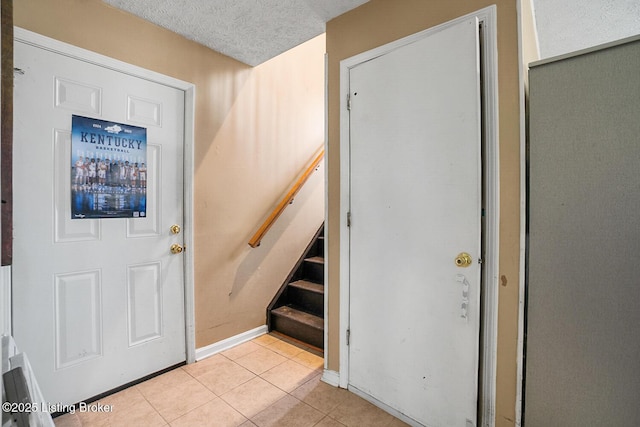 foyer entrance featuring stairway, a textured ceiling, baseboards, and light tile patterned floors