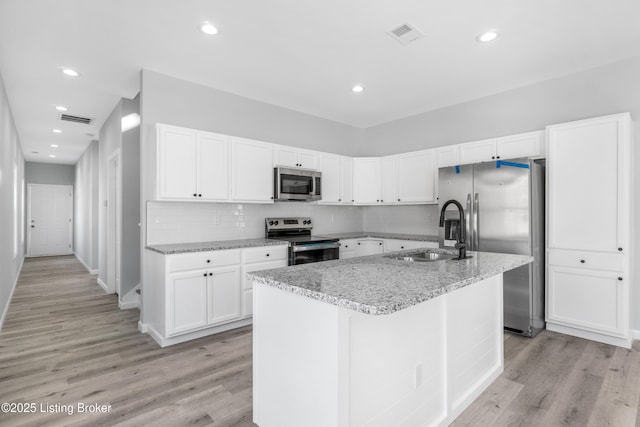 kitchen featuring appliances with stainless steel finishes, sink, light wood-type flooring, white cabinets, and an island with sink