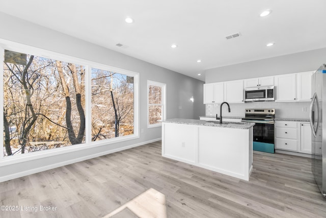 kitchen with a kitchen island with sink, stainless steel appliances, light stone countertops, white cabinets, and decorative backsplash