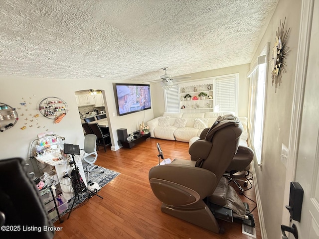 living area featuring a textured ceiling, wood finished floors, and a ceiling fan