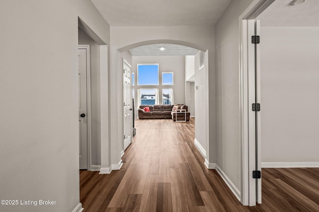 corridor featuring dark wood-type flooring, arched walkways, a textured ceiling, and baseboards