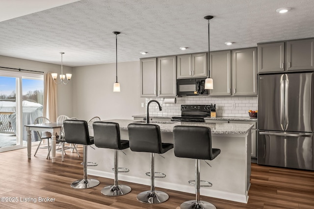 kitchen featuring light stone counters, a kitchen island with sink, gray cabinetry, dark wood-type flooring, and black appliances