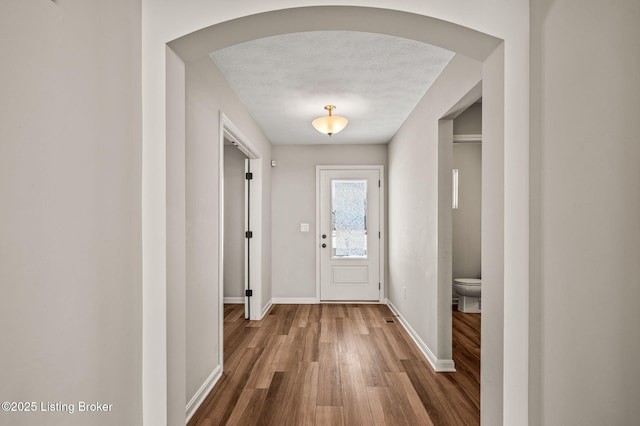 entryway featuring arched walkways, wood finished floors, baseboards, and a textured ceiling