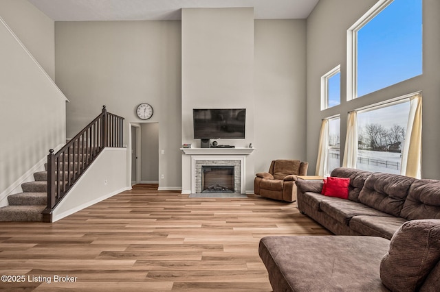living area featuring baseboards, light wood-style flooring, a high ceiling, stairs, and a fireplace with flush hearth