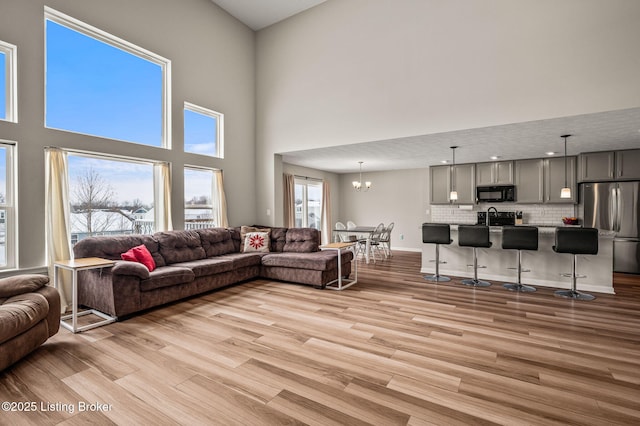 living area with a chandelier, light wood-style floors, baseboards, and a high ceiling