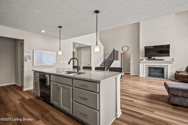 kitchen featuring open floor plan, gray cabinetry, dishwasher, a sink, and wood finished floors