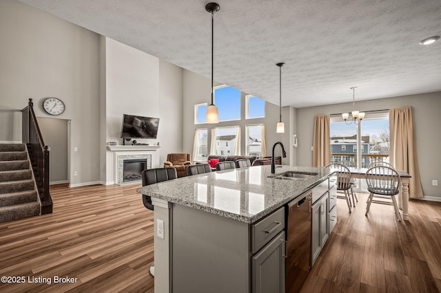 kitchen with dishwashing machine, a glass covered fireplace, gray cabinets, wood finished floors, and a sink