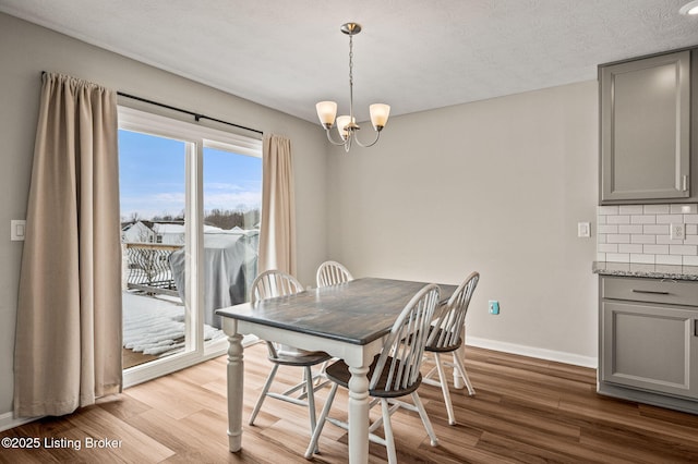dining room featuring a textured ceiling, wood finished floors, an inviting chandelier, and baseboards
