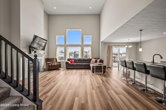 living area featuring a towering ceiling, baseboards, a chandelier, stairway, and light wood-style flooring