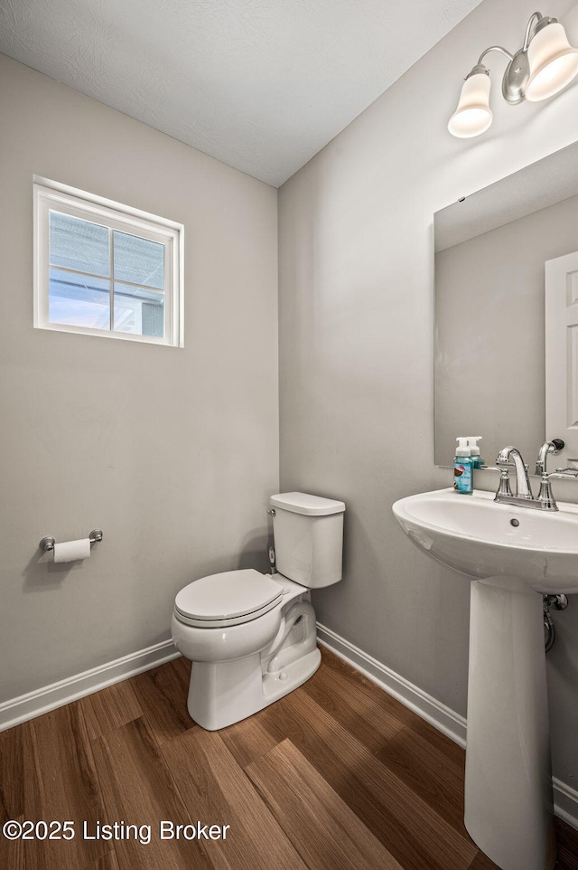 half bath with toilet, wood finished floors, a sink, and baseboards