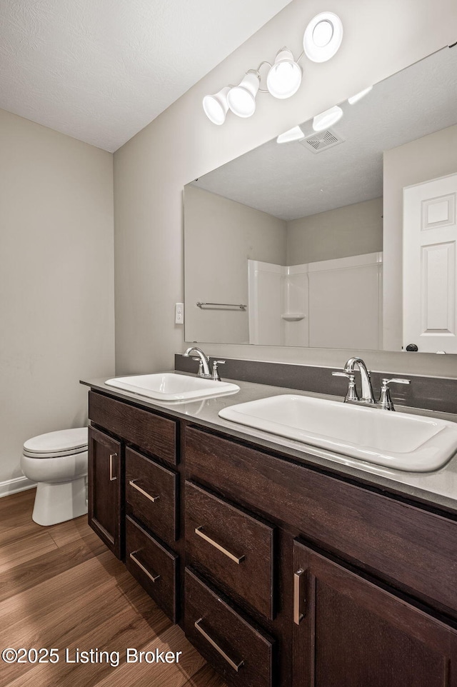 full bath featuring a sink, toilet, double vanity, and wood finished floors