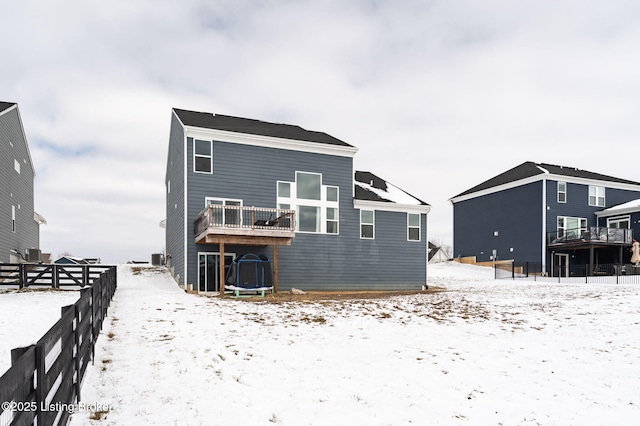 snow covered back of property with a trampoline, a deck, and fence