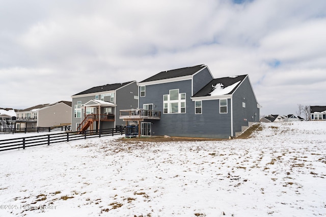 snow covered rear of property featuring a residential view, a wooden deck, and fence