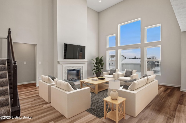 living area with light wood-style flooring, a towering ceiling, a fireplace, and stairs