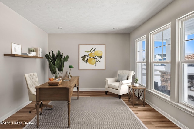 office with light wood-style floors, baseboards, and a textured ceiling
