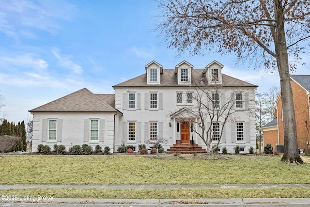 view of front facade with a shingled roof, a front lawn, and brick siding