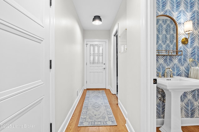 corridor featuring wallpapered walls, baseboards, an accent wall, wood finished floors, and a sink