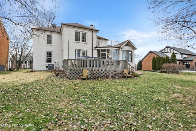 rear view of house with cooling unit, brick siding, a lawn, a wooden deck, and a chimney