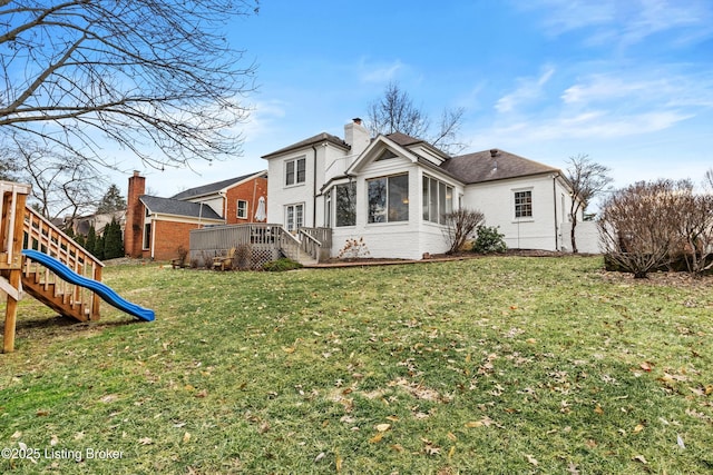 back of property with a playground, brick siding, a lawn, and a chimney